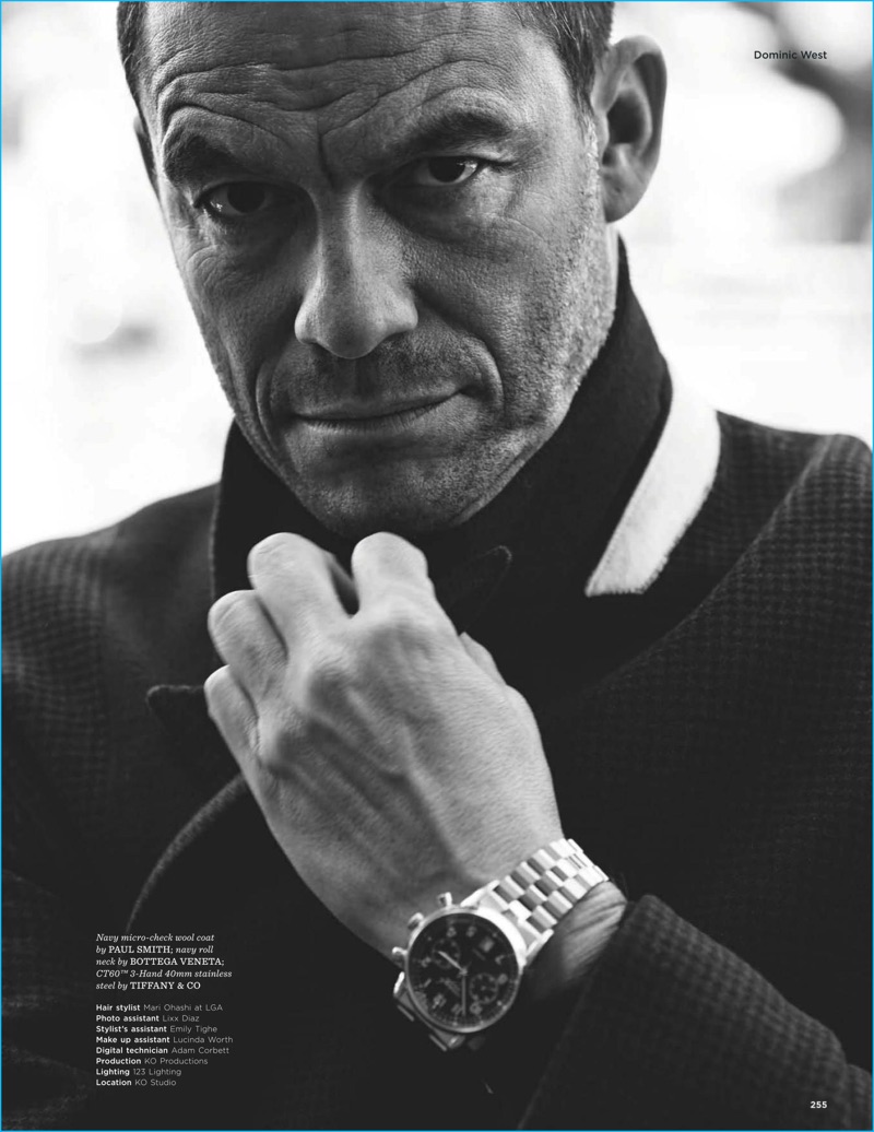 Dominic West captured in a black & white photo, wearing a micro-check wool coat from Paul Smith with a Bottega Veneta knit and Tiffany & Co. watch.