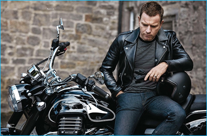 Ewan McGregor poses on a motorcycle, sporting a Tom Ford leather biker jacket, Acne Studios denim jeans, and Fratelli Orsini gloves with a striped t-shirt from Saint Laurent.