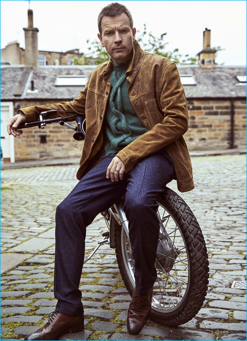 Ewan McGregor pictured in a brown leather shirt jacket from Timberland with a green deconstructed cable knit Etro sweater, Canali trousers, and brown Tod's leather shoes.