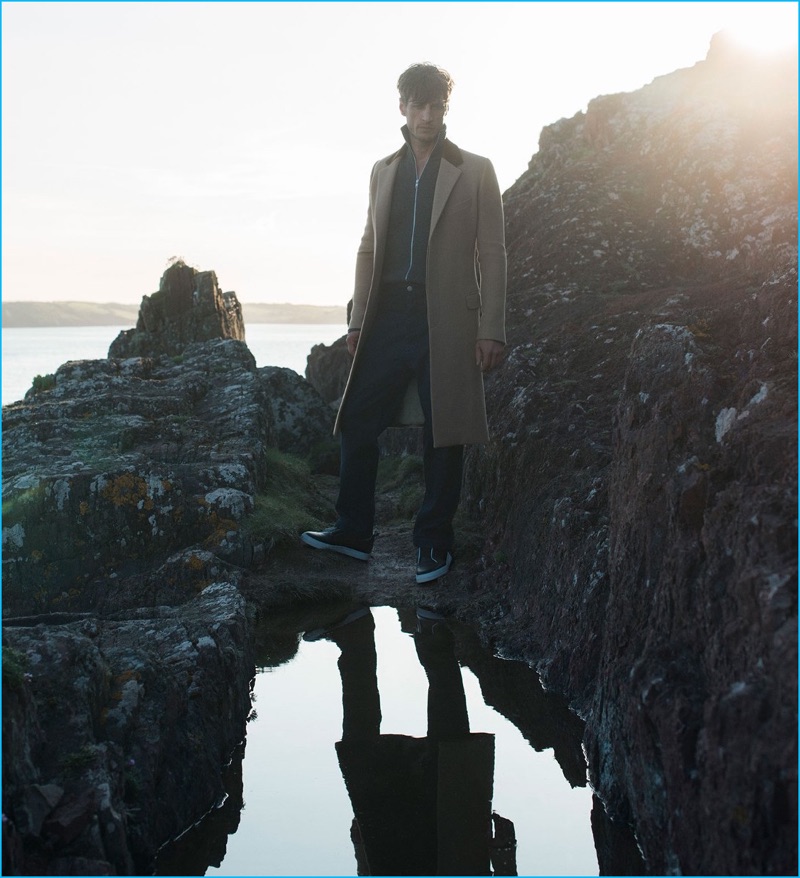 Axel Hermann wears camel wool coat Alexander McQueen, full-zip sweater Burberry, tailored denim trousers Raey, and leather sneakers Pierre Hardy.