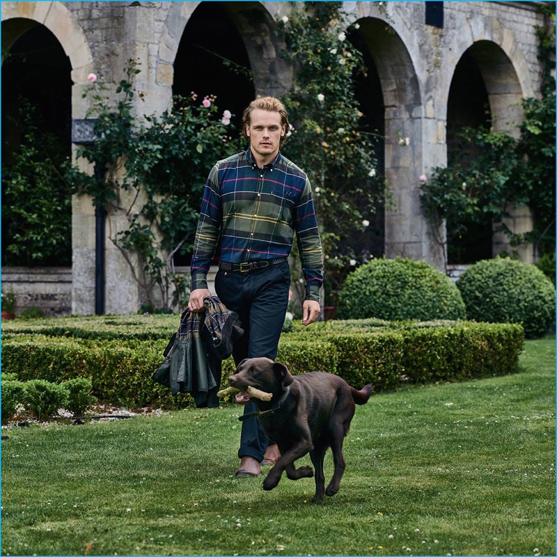 Sam Heughan wears a blue and green tartan shirt from Barbour.