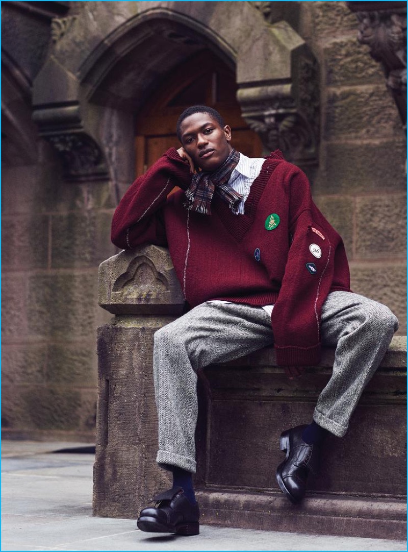 Hamid Onifade models herringbone trousers and dress shoes Ermenegildo Zegna Couture, oversized burgundy sweater, striped shirt, and plaid scarf Raf Simons.