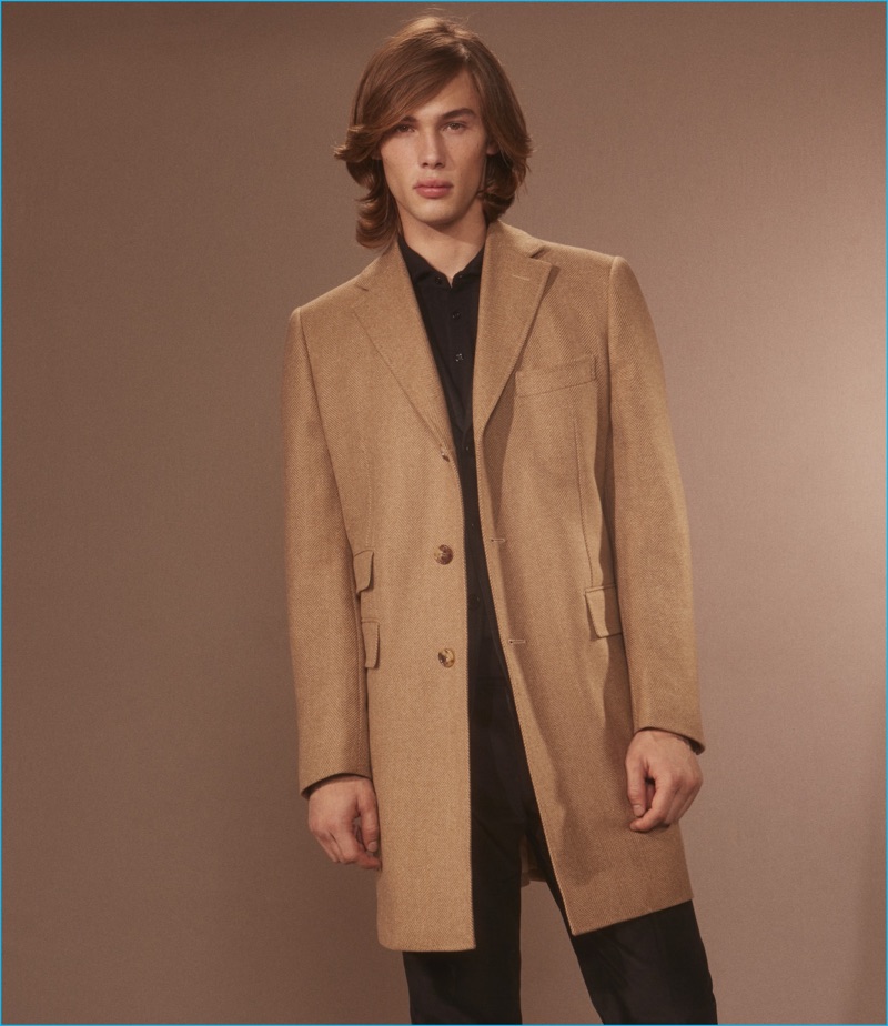 Embracing classic tailoring, Anders Donatelli wears a single-breasted camel coat, wool flannel two-button sport coat, cashmere long sleeve polo shirt, and corduroy trousers from Cifonelli.