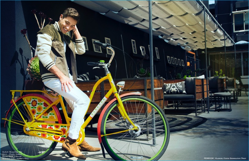 Posing on a bicycle, Gabriel Conte wears a Beautiful Fül varsity jacket with pants and shoes from Saint Laurent for Ferrvor.