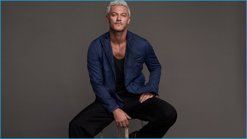 Sitting for a portrait, Luke Evans wears a blue Bottega Veneta double-breasted blazer, Acne Studios cotton jersey t-shirt, Balenciaga wide-leg trousers, and Lanvin leather sneakers.