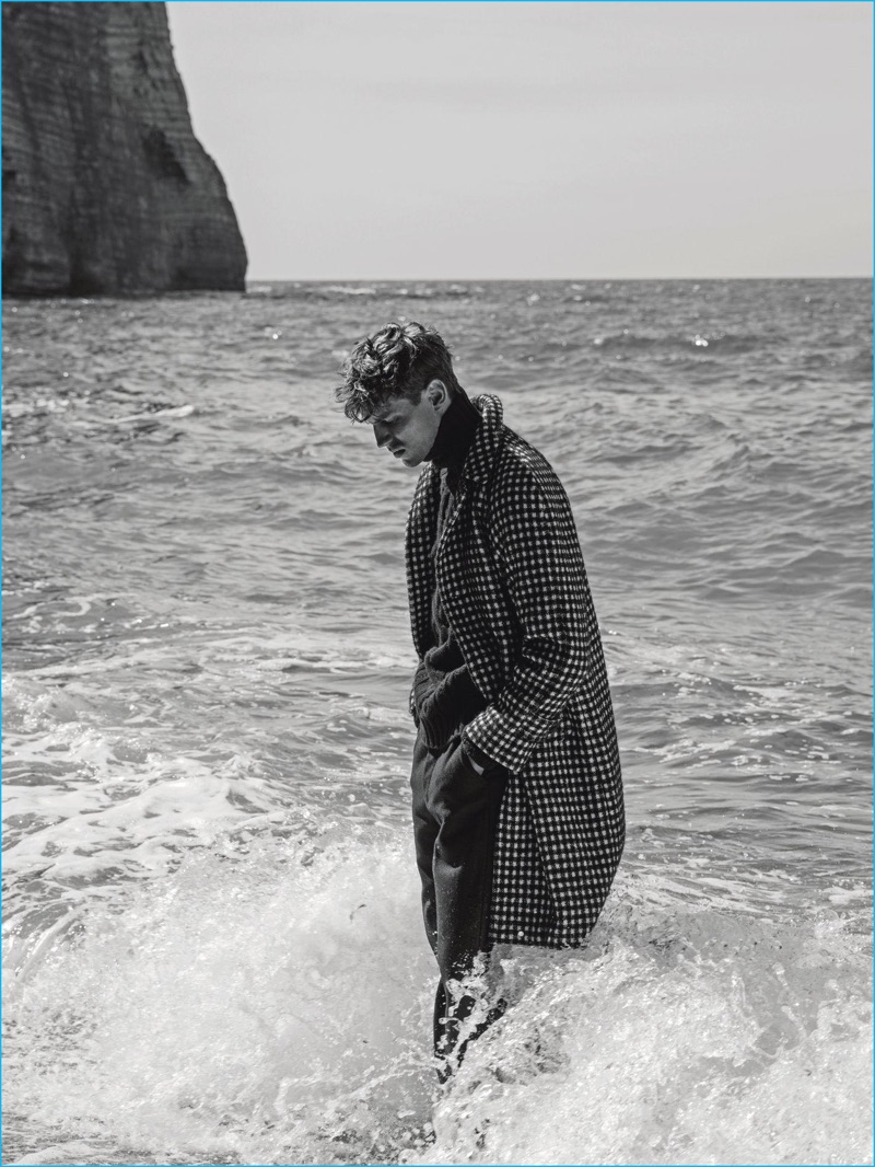 Model Victor Norlander steps into the tide, wearing a check Sandro coat, Eric Bompard sweater, and Paul & Joe trousers.