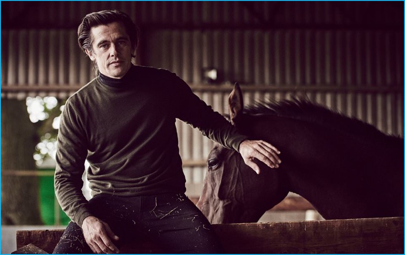 Posing with a horse, Werner Schreyer wears a cashmere turtleneck, sweater, and slim-fit denim jeans from Ralph Lauren Purple Label.