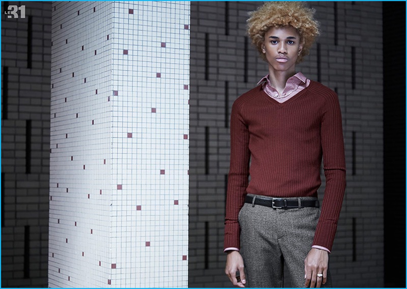 Channeling a retro flair, Michael Lockley dons a red ribbed-knit v-neck sweater, brown tailored shirt, and micro-houndstooth trousers from LE 31.