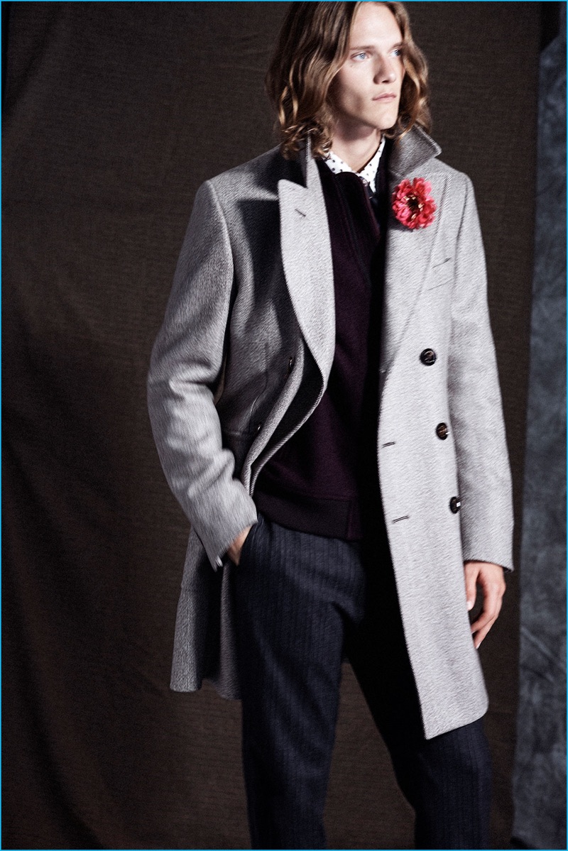 Ryan Keating wears a herringbone topcoat, wool bomber jacket, foulard shirt, tie, and striped trousers from Club Monaco.