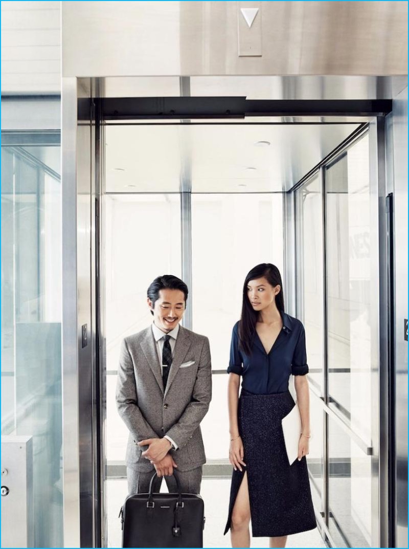 All smiles, Steven Yeun sports an Isaia suit with a John Varvatos Star USA shirt, Thomas Mason tie, a pocket square by The Tie Bar, and a Louis Vuitton briefcase.
