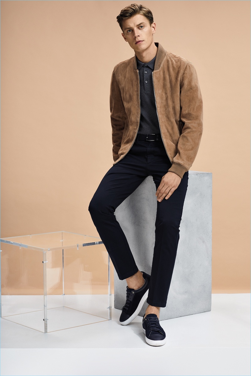 Leading model Janis Ancens sports a suede bomber jacket with a polo shirt, slim-fit pants, and sneakers by BOSS Hugo Boss.