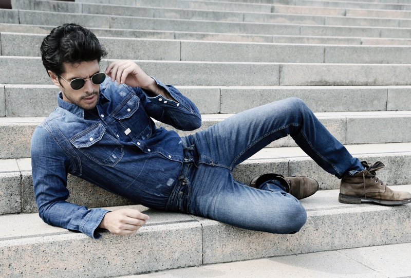 Raul wears denim shirt G-Star Raw, distressed denim jeans GUESS, boots Replay, and aviator sunglasses Ray-Ban.