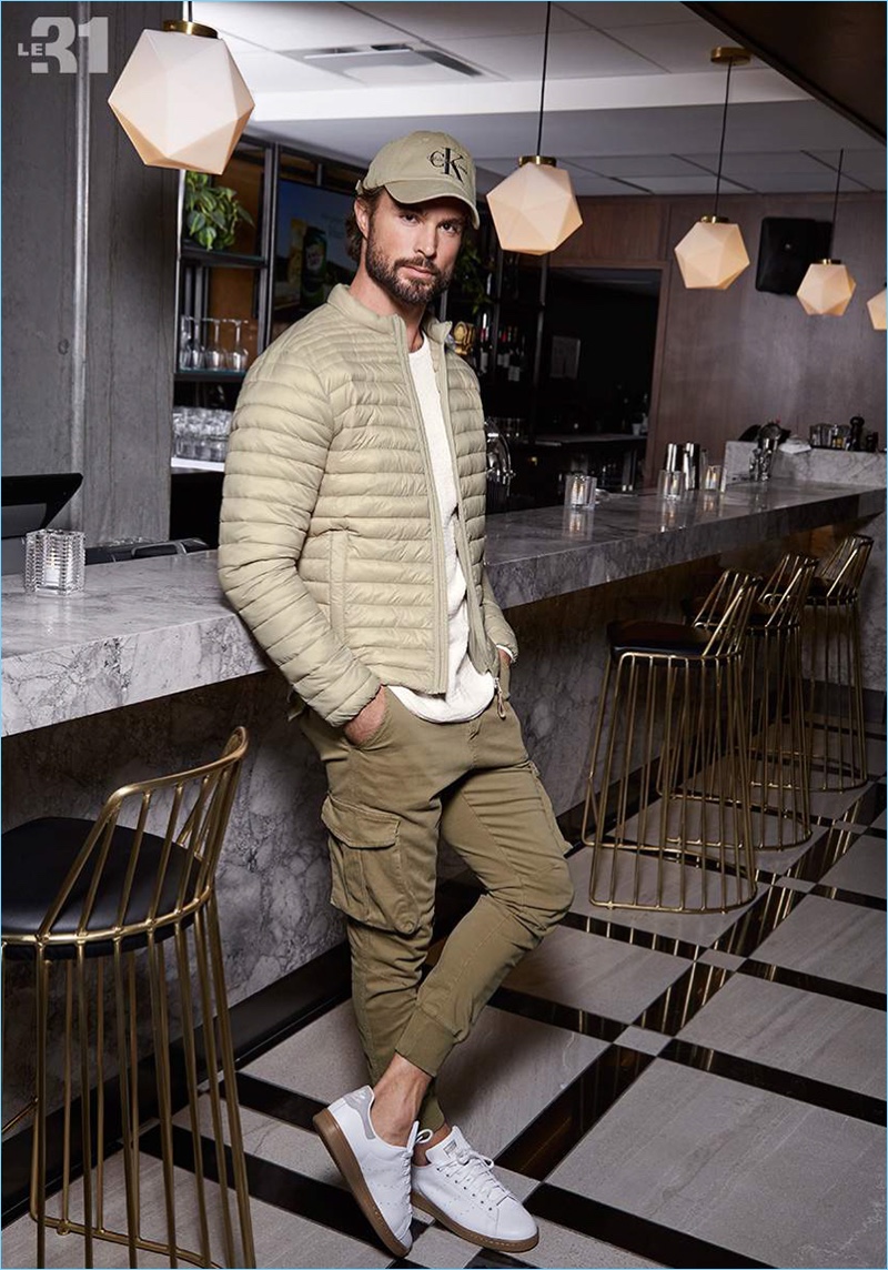 Monochromatic style is front and center as Walter Savage wears a LE 31 quilted jacket, knit sweater, and cargo joggers with a Calvin Klein logo cap. Walter also sports Adidas' essential Stan Smith sneakers.