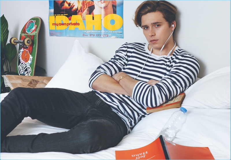 Lounging in bed, Brooklyn Beckham wears a Burberry striped tee with Saint Laurent jeans. Brooklyn also wears Beats headphones and Cartier bracelets.