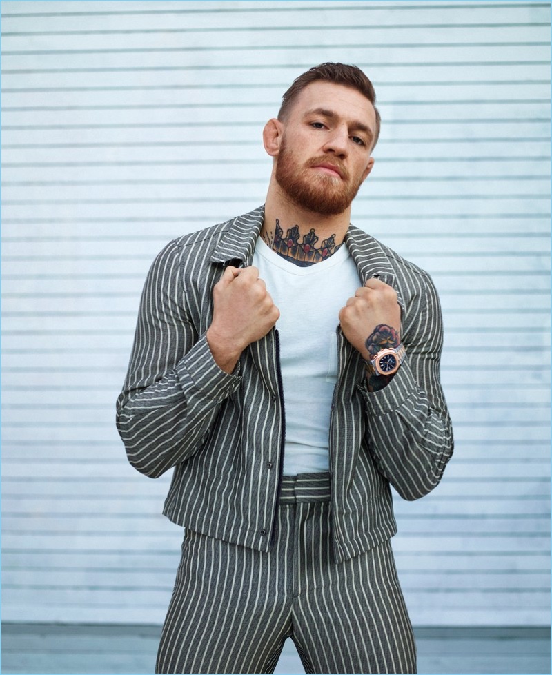 Conor McGregor dons a Salvatore Ferragamo pinstripe suit with a Tom Ford shirt, Santoni loafers, and a Patek Philippe watch.
