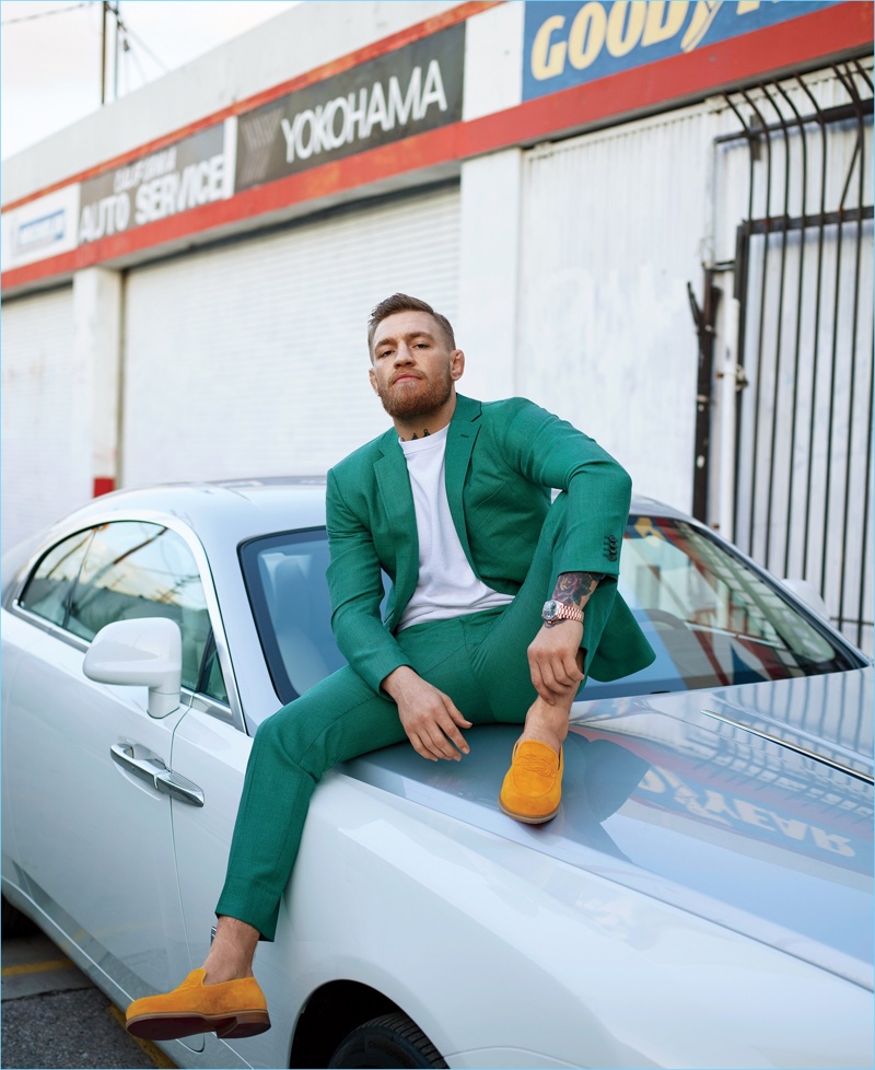 Sitting on a Rolls-Royce Wraith, Conor McGregor wears a custom green suit by David August Couture. McGregor also dons a Velva Sheen sweatshirt with Christian Louboutin loafers.
