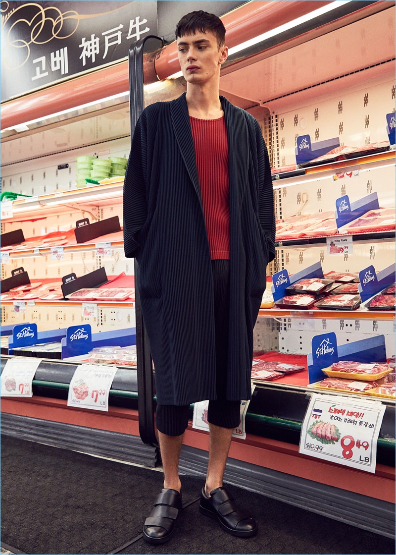Embracing a draped silhouette, Simon Kotyk dons an Issey Miyake Homme Plisse long jacket with a red shirt and pleated cropped trousers. Simon's look is complete with Acne Studios leather sneakers.