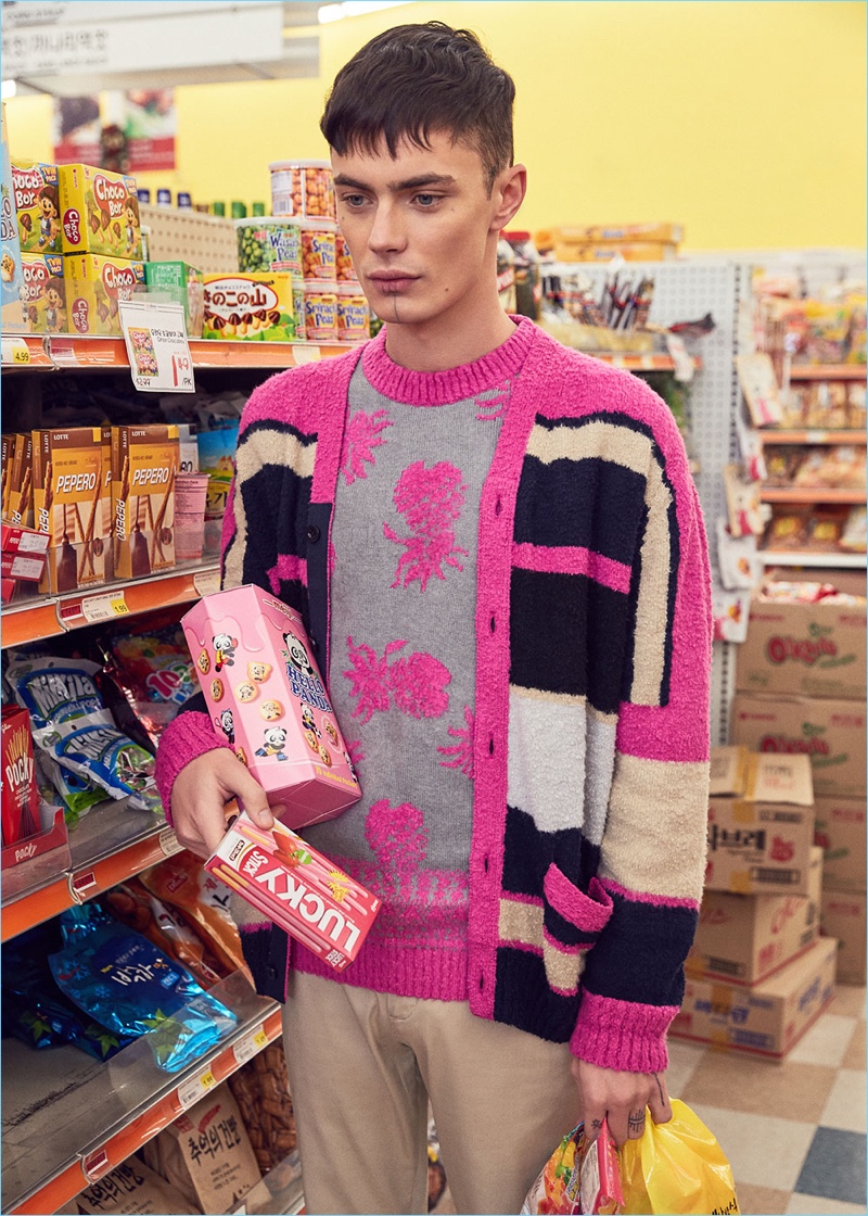 Making a statement in pink, Simon Kotyk wears a Sacai stripe knit cardigan and pineapple knit pullover. Embracing basics for the rest of his look, Simon dons Acne Studios satin trousers.