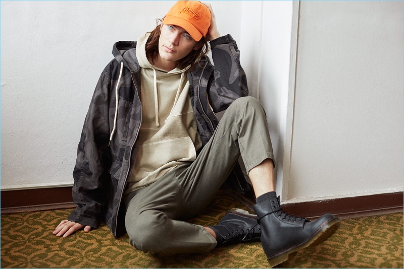 Model Jaco van den Hoven layers in a hoodie, camouflage print jacket, and twill pants with combat boots.