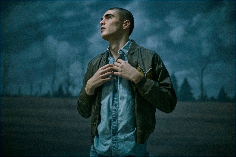 Appearing in a moody image, Diego Villarreal sports a bomber jacket, chambray shirt, and jeans from RRL.