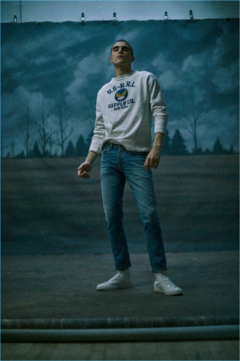 Embracing an all-American flair, Diego Villarreal wears a RRL logo fleece sweatshirt and denim jeans with Comme des Garçons Play sneakers.