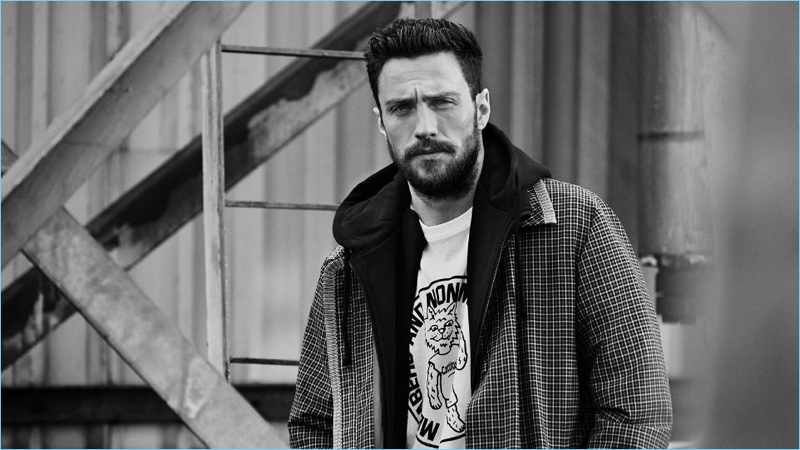Aaron Taylor-Johnson sports a Prada checked wool coat with a Vetements + Champion hoodie and a Stella McCartney graphic t-shirt.