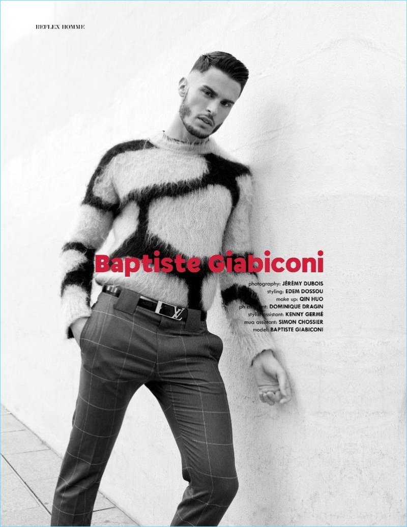 French model Baptiste Giabiconi dons a giraffe print sweater with windowpane print trousers and a logo belt by Louis Vuitton.