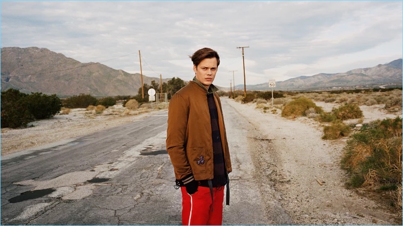 Bill Skarsgård wears a Lanvin bomber jacket with a sweater by The Soloist. Skarsgård also wears a Kent & Curwen shirt with Gucci trousers.