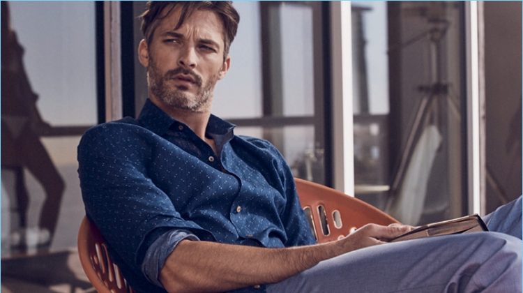Relaxing, Ben Hill wears trousers and a navy chambray shirt with a star print from J.Hilburn.
