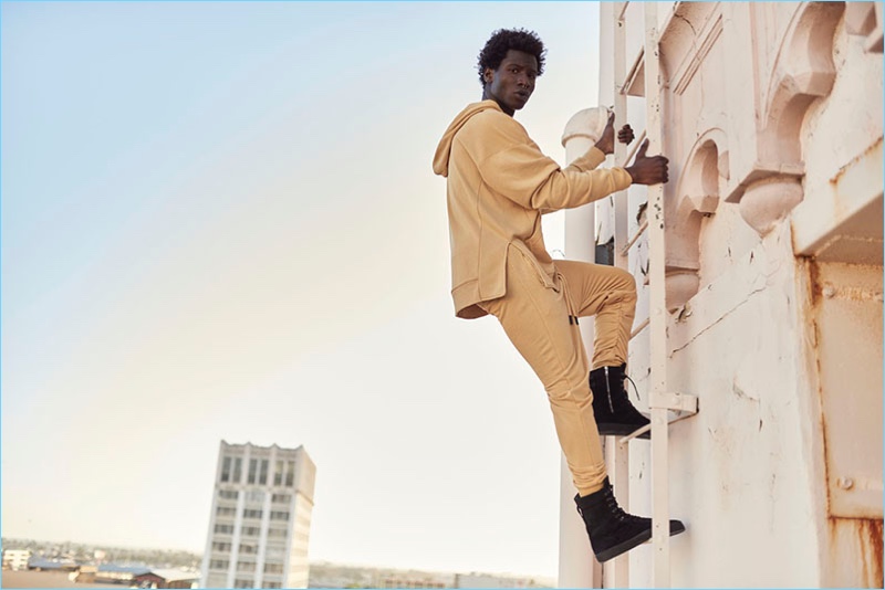 Climbing a ladder, Adonis Bosso wears joggers and a hoodie from Other UK's OTHERSIDE collection.