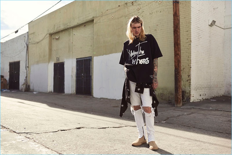Pictured in an alley, Bradley Soileau wears an oversized t-shirt and ripped white jeans from Other UK.