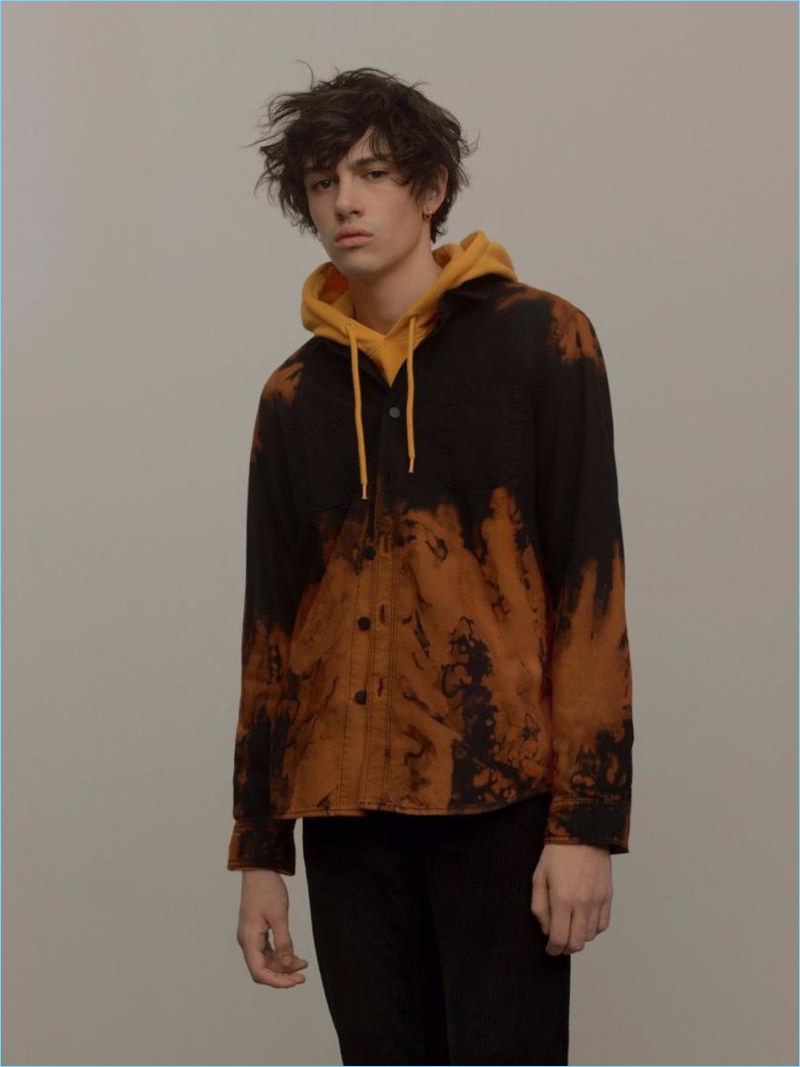 Going casual, Basti Robert wears a mustard yellow overhead hoodie with a black and orange sunset denim shirt by Topman.