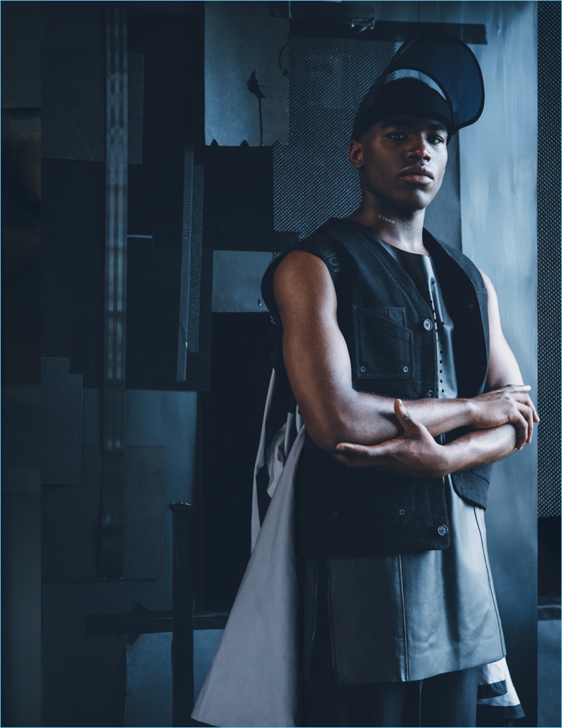 Taking a confident stance, Ike Nwachukwu wears a Y-3 vest, cape, and hat with McQ by Alexander McQueen pants.