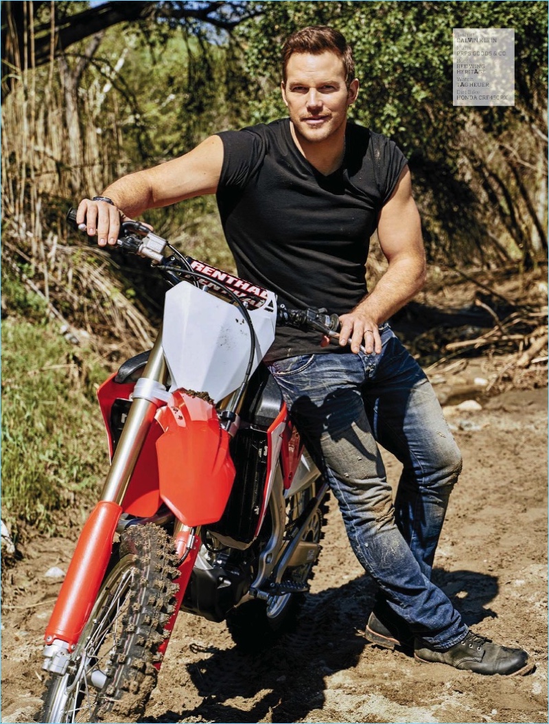 Posing on a dirt bike, Chris Pratt sports a Calvin Klein t-shirt, PRPS Goods & co jeans, Red Wing Heritage boots, and a TAG Heuer watch.