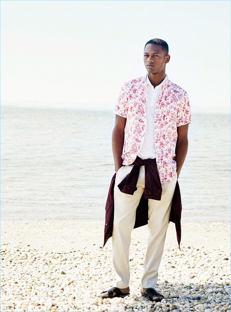 Taking to the beach, Lucas Cristino wears a Club Monaco tech car coat $249, floral print linen shirt $98.50, polo $69.50, linen pants $169.50, and sandals $260.
