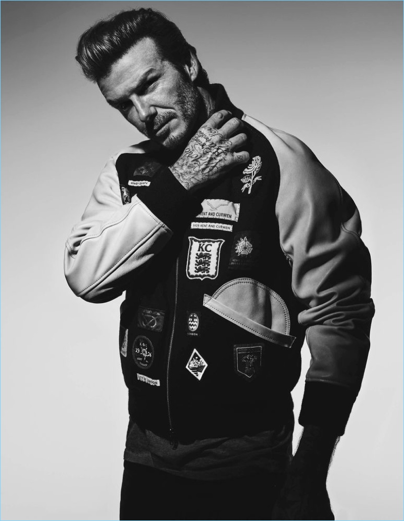 Front and center, David Beckham wears a Kent & Curwen varsity bomber jacket, Balmain t-shirt, and Saint Laurent jeans.