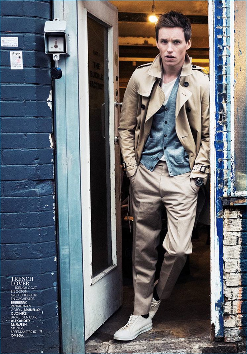 A stylish vision, Eddie Redmayne wears a Burberry trench coat, tee, and cardigan sweater. Redmayne also sports Brunello Cucinelli pants and Alexander McQueen sneakers.