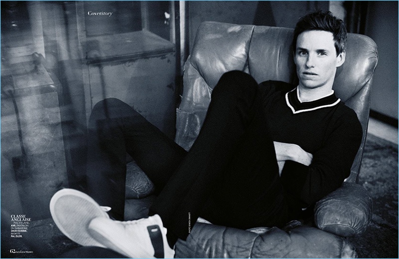 Relaxing, Eddie Redmayne dons an AMI v-neck sweater with Dior Homme pants, and Pal Zileri sneakers.