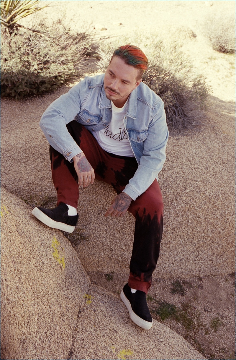 Taking to the desert, J Balvin wears an Ovadia & Sons Type-01 light washed indigo denim jacket $375, Paradise oversized shirt $125, and tie-dye sweats $225.