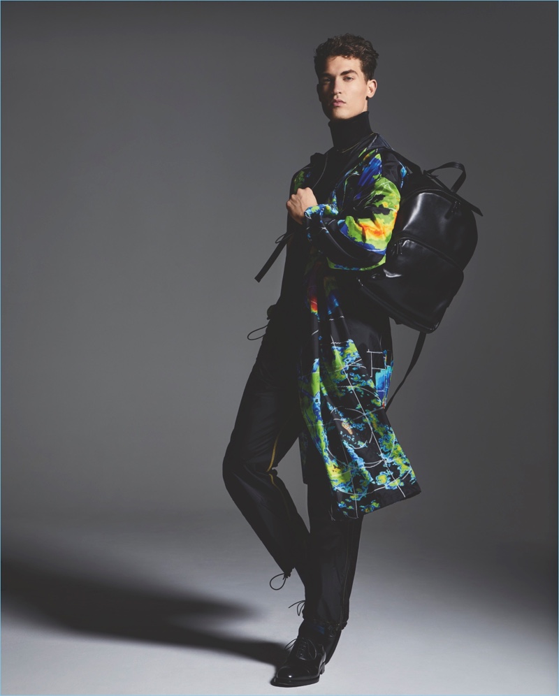 Michelle Holden photographs Jason Anthony in a Prada digital print nylon coat, vest, wool sweater, nylon trousers, leather shoes, and backpack.