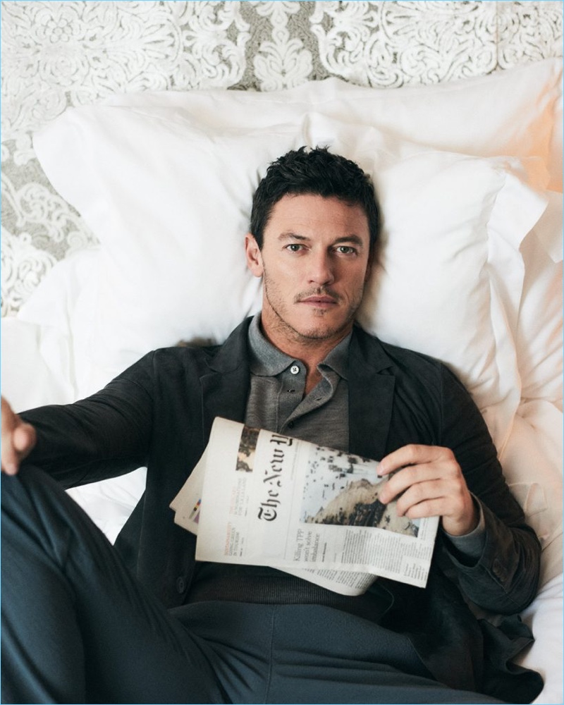 Lounging in bed, Luke Evans wears a Hardy Amies polo with a grey blazer and trousers by Giorgio Armani.