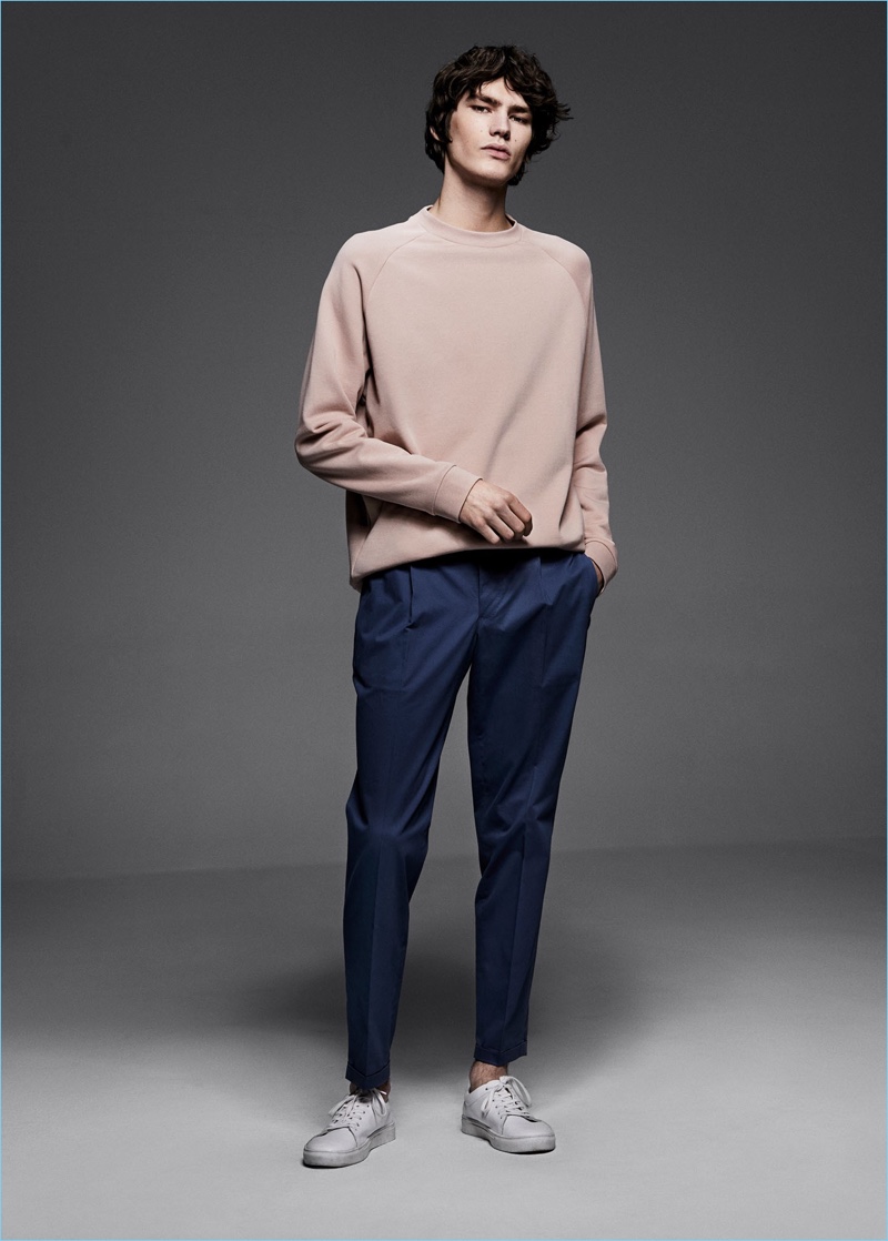 Embracing a casual look, Elias de Poot dons a Mango Man pink sweatshirt $49.99, slim-fit cotton suit trousers $89.99, and canvas sneakers $35.99.