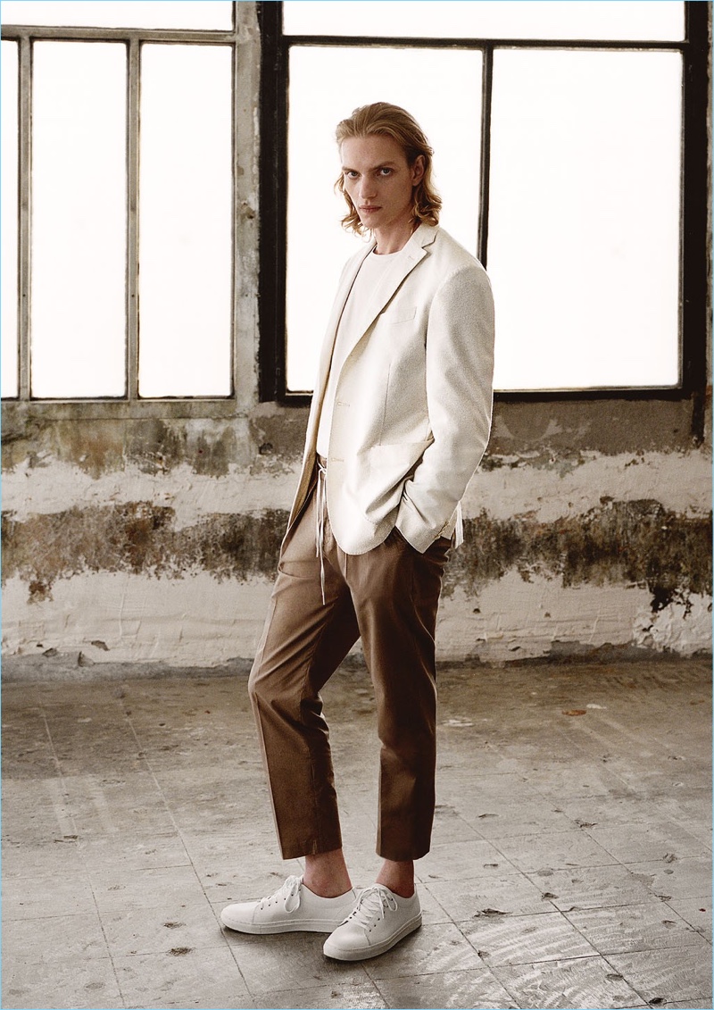 Model Paul Boche embraces a neutral color palette. He wears a Mango Man slim-fit textured blazer $199.99, v-neck t-shirt $15.99, pleated trousers $69.99, and lace-up leather sneakers $69.99.