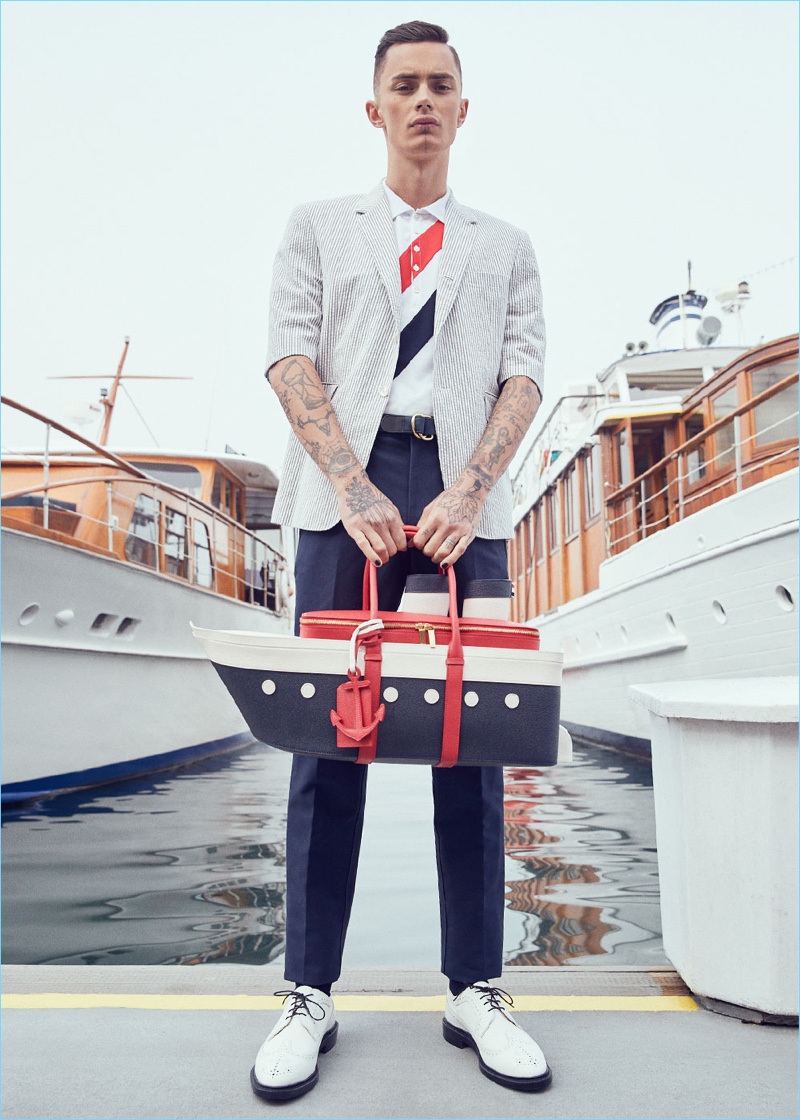 Embracing preppy nautical-inspired styles, Simon Kotyk wears a Thom Browne short-sleeve seersucker blazer $1,850, diagonal stripes polo $590, unconstructed chino pants $395, and contrast longwing leather brogues $1,250. Simon also sports a Thom Browne cruise liner bag $2,700 and multicolor fun mix D ring belt $490.