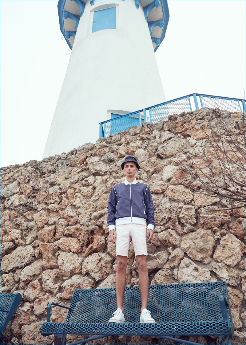 Nautical style is front and center as Simon Kotyk wears a Thom Browne double-sided bomber jacket $990, cashmere polo $1,490, and lightweight twill shorts $780. The Czech model also wears Thom Browne pebble grain trainers $590 and a lined bucket hat $175.