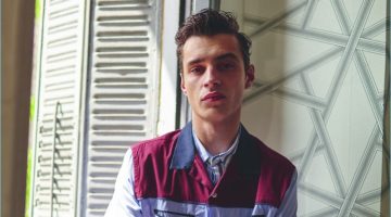 Crossing his arms, Adrien Sahores wears a striped Wrangler shirt with an Andrea Pompilio short-sleeve shirt. The French model also wears Salvatore Ferragamo trousers and a Hamilton watch.
