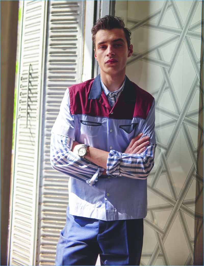 Crossing his arms, Adrien Sahores wears a striped Wrangler shirt with an Andrea Pompilio short-sleeve shirt. The French model also wears Salvatore Ferragamo trousers and a Hamilton watch.