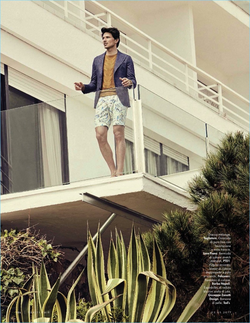 Pictured on a balcony, Andres Velencoso wears a Tagliatore blazer, Loro Piana sweater, and PT01 shorts.