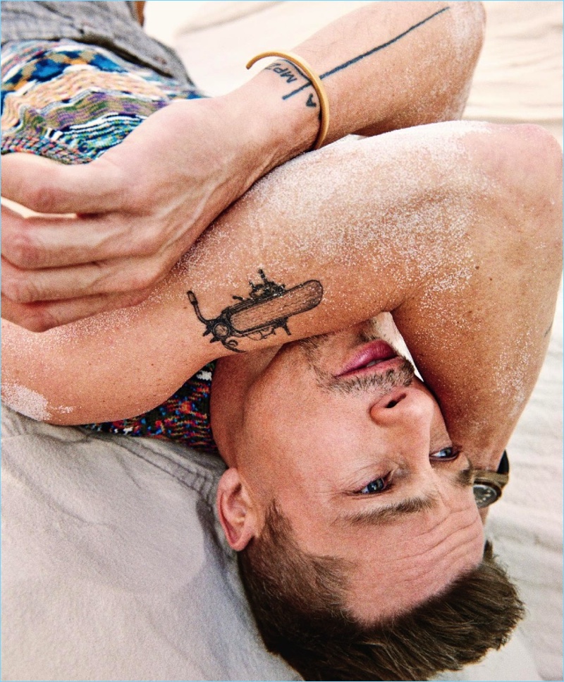 Laying down, Brad Pitt wears a Missoni sweater vest with Giorgio Armani pants, a Tudor watch, and a Miansai bracelet.