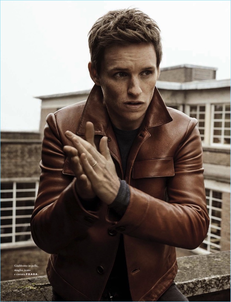 Clad in Prada, Eddie Redmayne wears a brown leather jacket, sweater, and denim jeans.